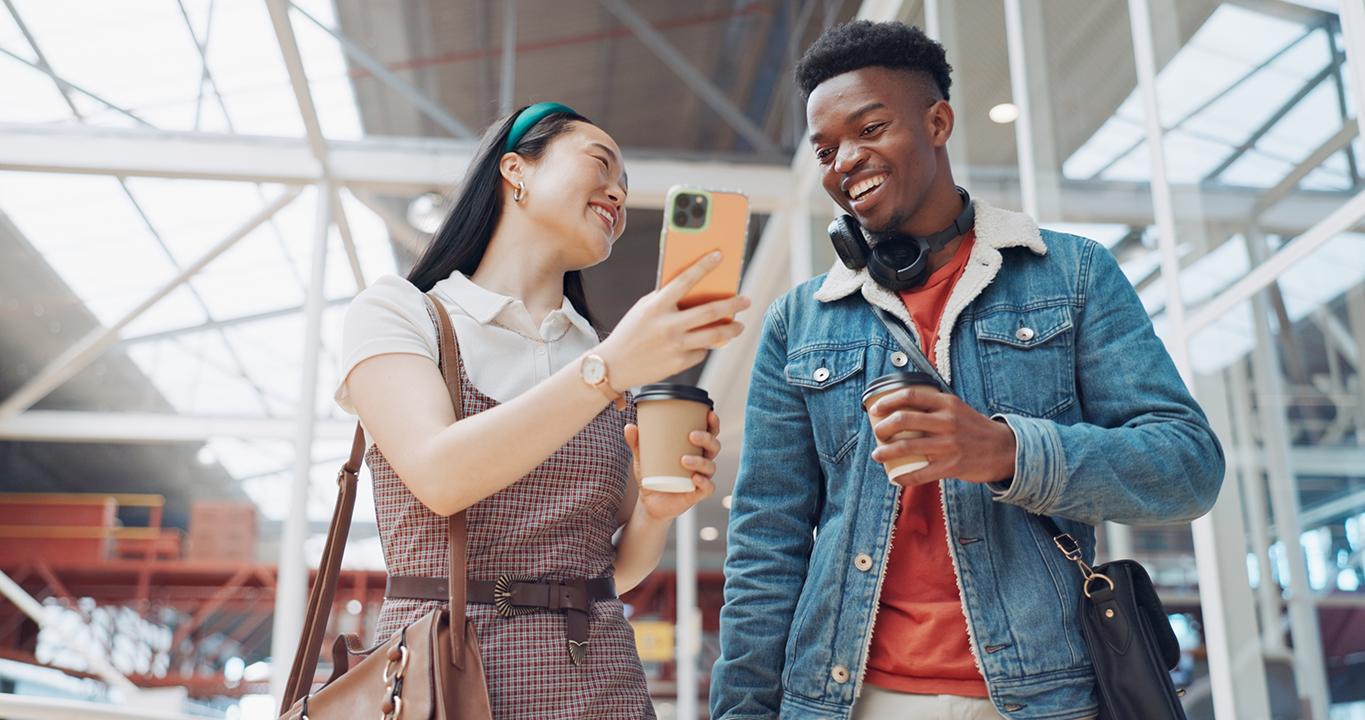 Two students smiling and looking at a smartphone, representing Rosetta Stone's language learning solutions for schools, promoting interactive and mobile learning.